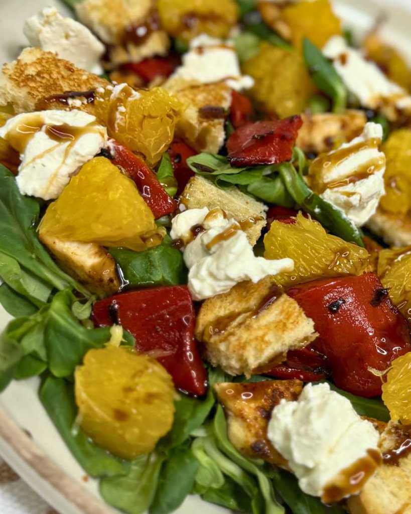 Close-up of healthy summer chicken salad with orange slices, roasted peppers, feta, croutons, and balsamic glaze on fresh greens