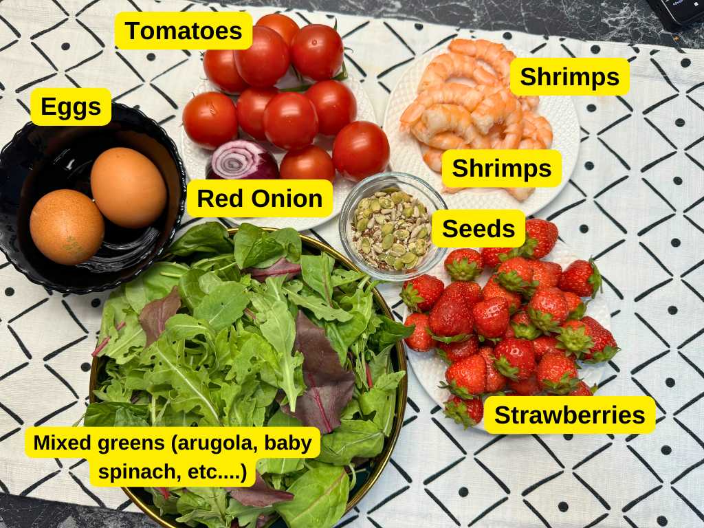 Fresh ingredients for shrimp salad including shrimps, strawberries, cherry tomatoes, red onion, mixed greens, eggs, and seed mix.