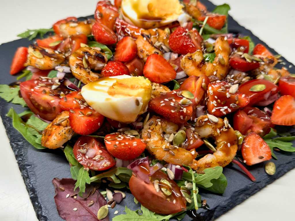 Sweet and savory shrimp salad with strawberries, cherry tomatoes, soft-boiled egg, mixed greens, seeds, and balsamic glaze