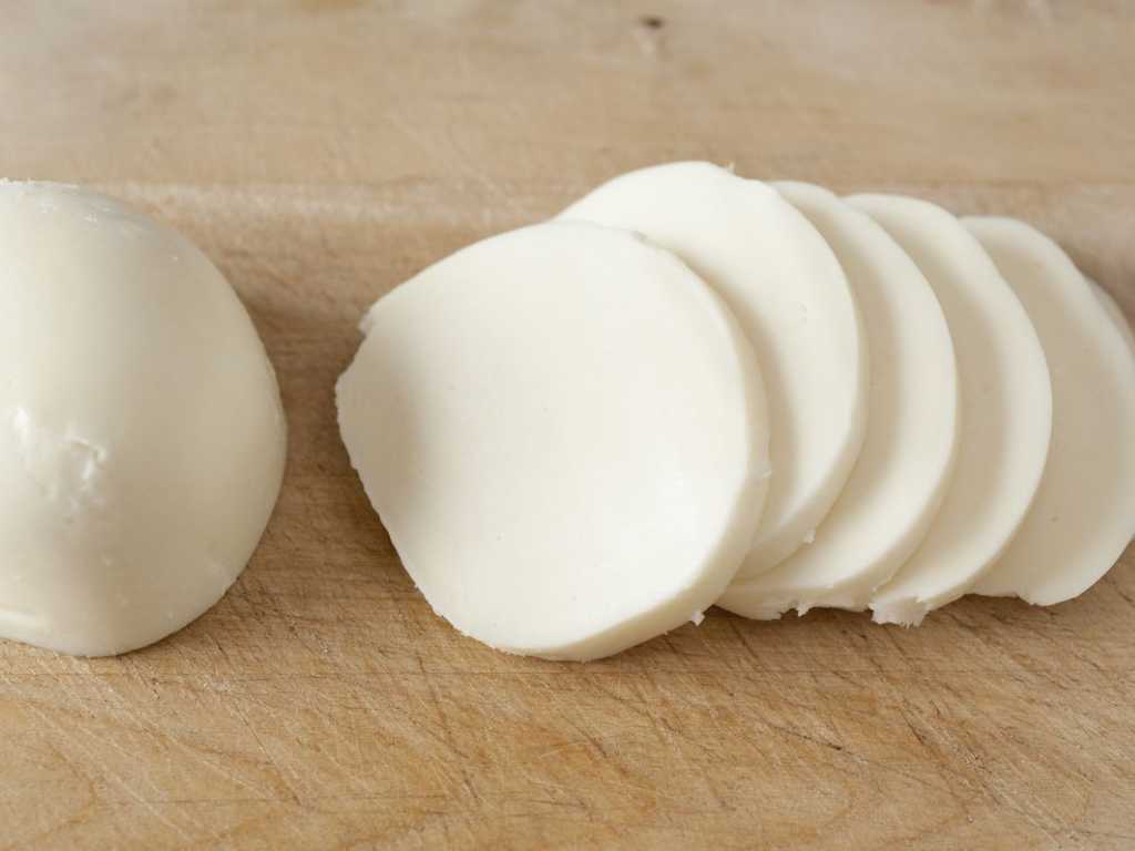 Fresh mozzarella sliced into even rounds on a wooden board, ready to be layered inside the chicken roulade.