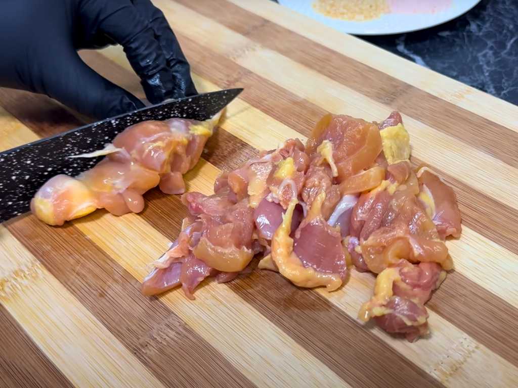 Cutting boneless chicken thighs into small pieces on a wooden board for cheesy quesadilla cones