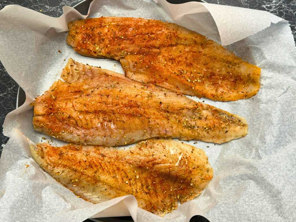 Seasoned cod fillets on parchment paper, coated with paprika, oregano, thyme, salt, and pepper before baking.