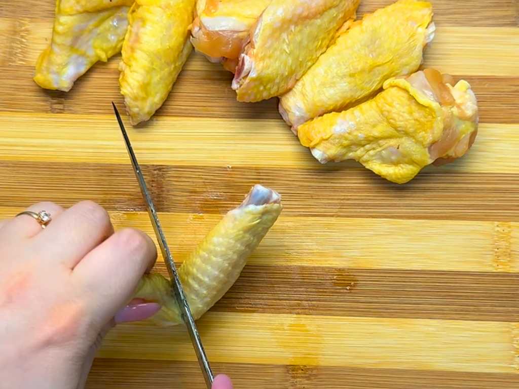 Cutting chicken wings on a wooden board to separate the drumettes and wing tips