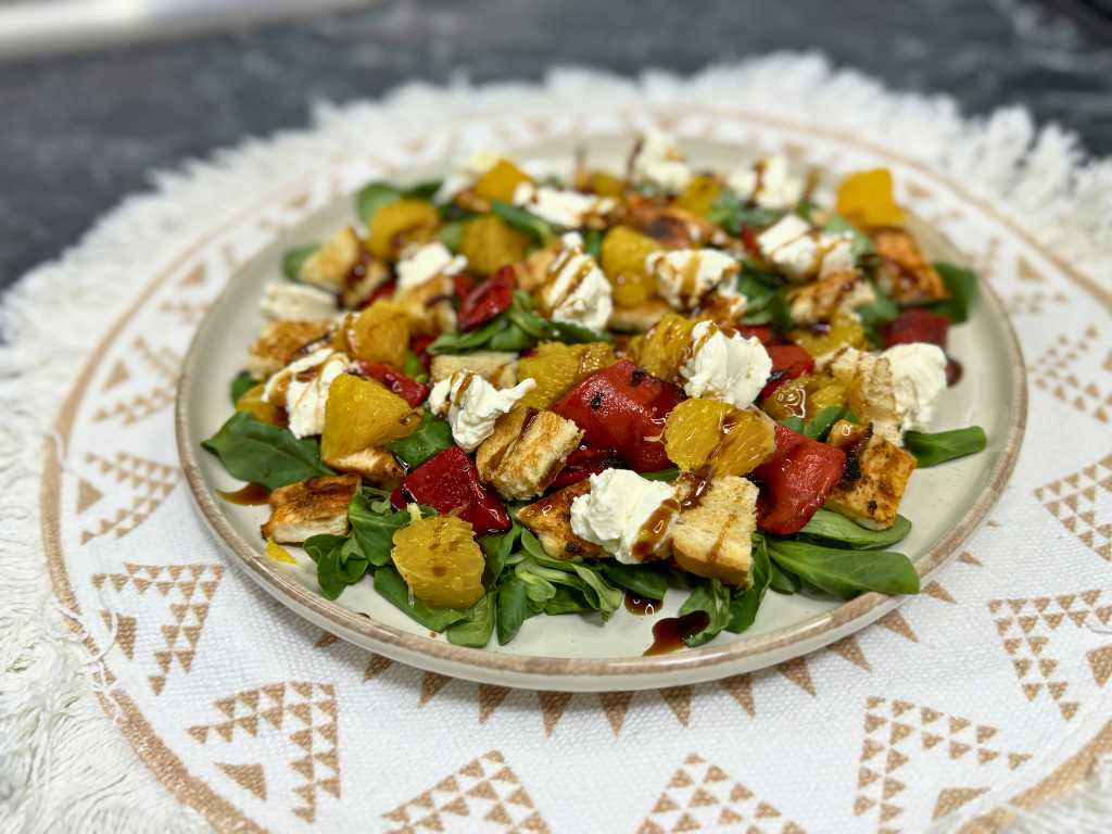 Plate of healthy summer chicken salad with orange slices, roasted red peppers, feta cheese, toasted bread cubes, and balsamic drizzle on fresh greens