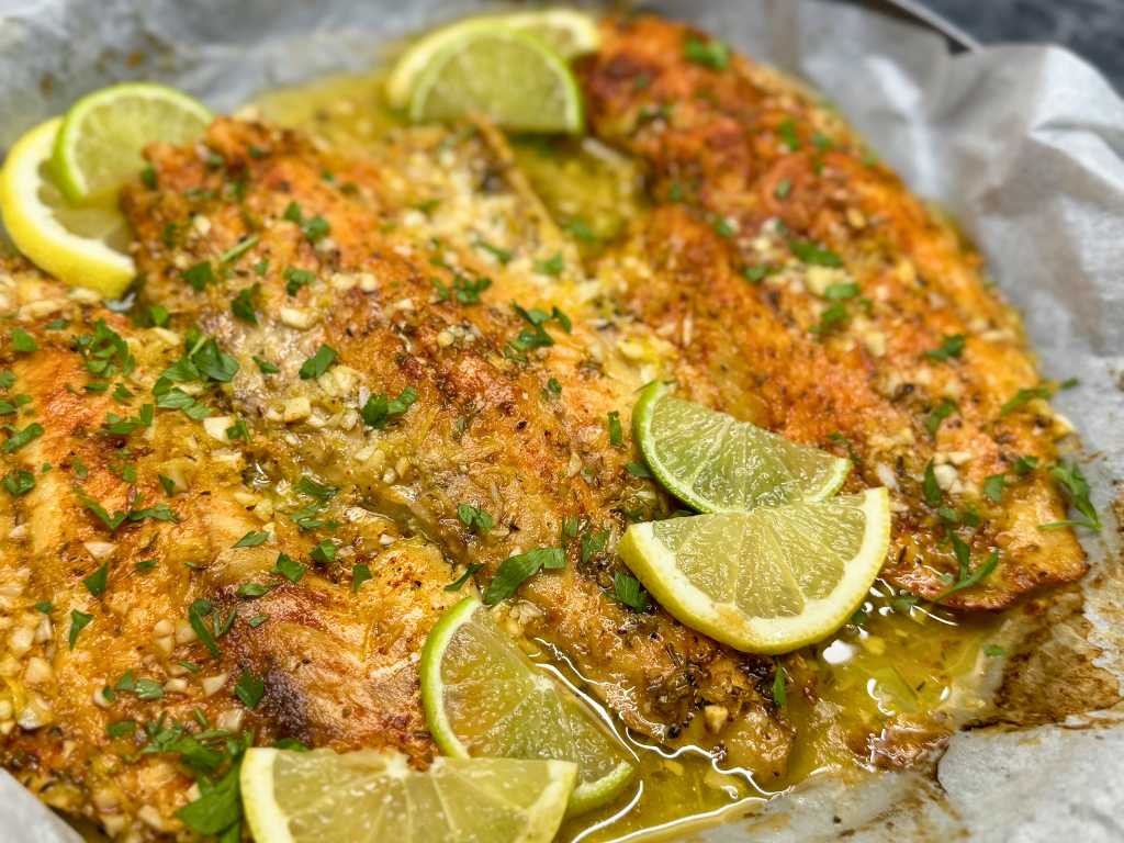 Oven-baked cod fillets in garlic lemon butter sauce, topped with fresh parsley and lemon slices.
