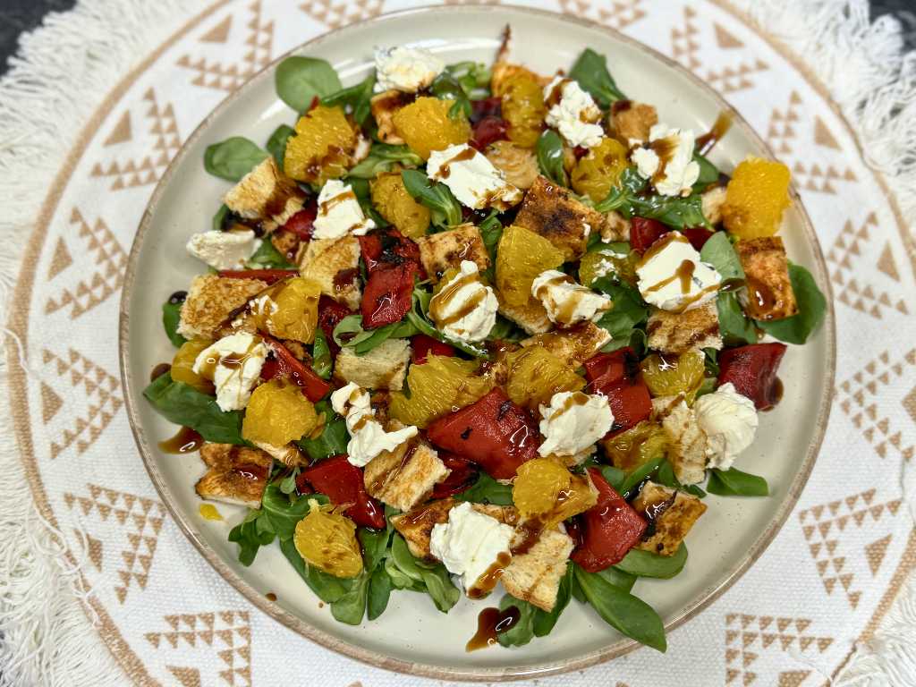 Healthy summer chicken salad with orange slices, roasted red peppers, feta, toasted bread cubes, fresh greens, and balsamic glaze on a plate