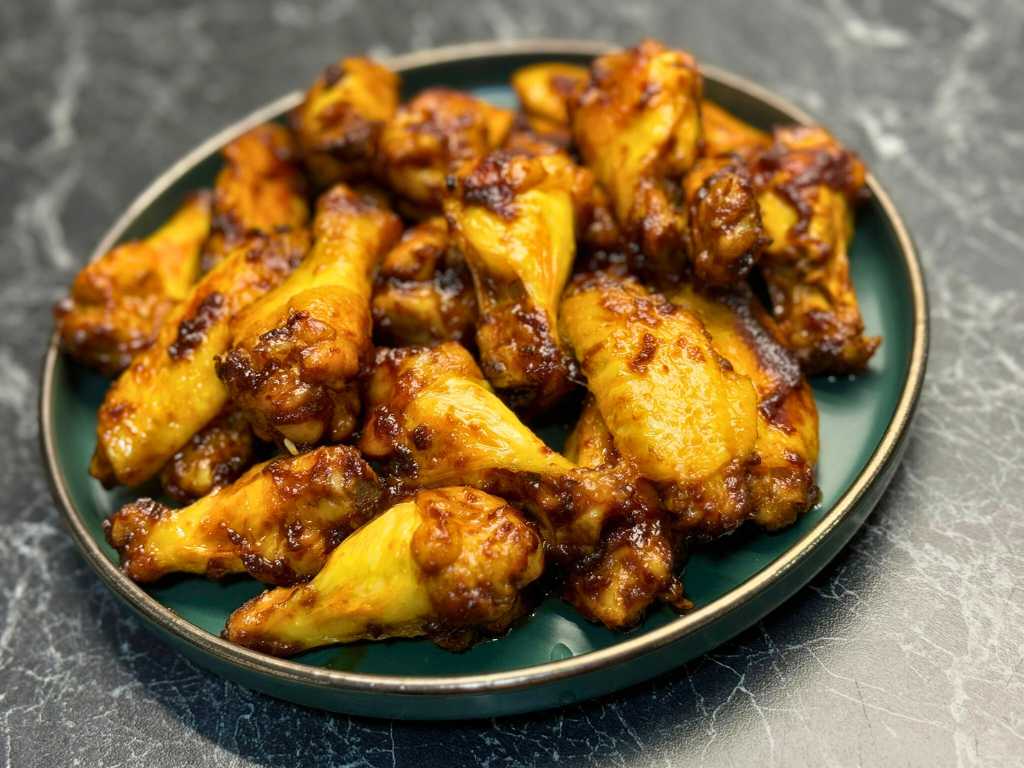Caramelized honey soy chicken wings served on a dark plate, coated in a sticky glaze