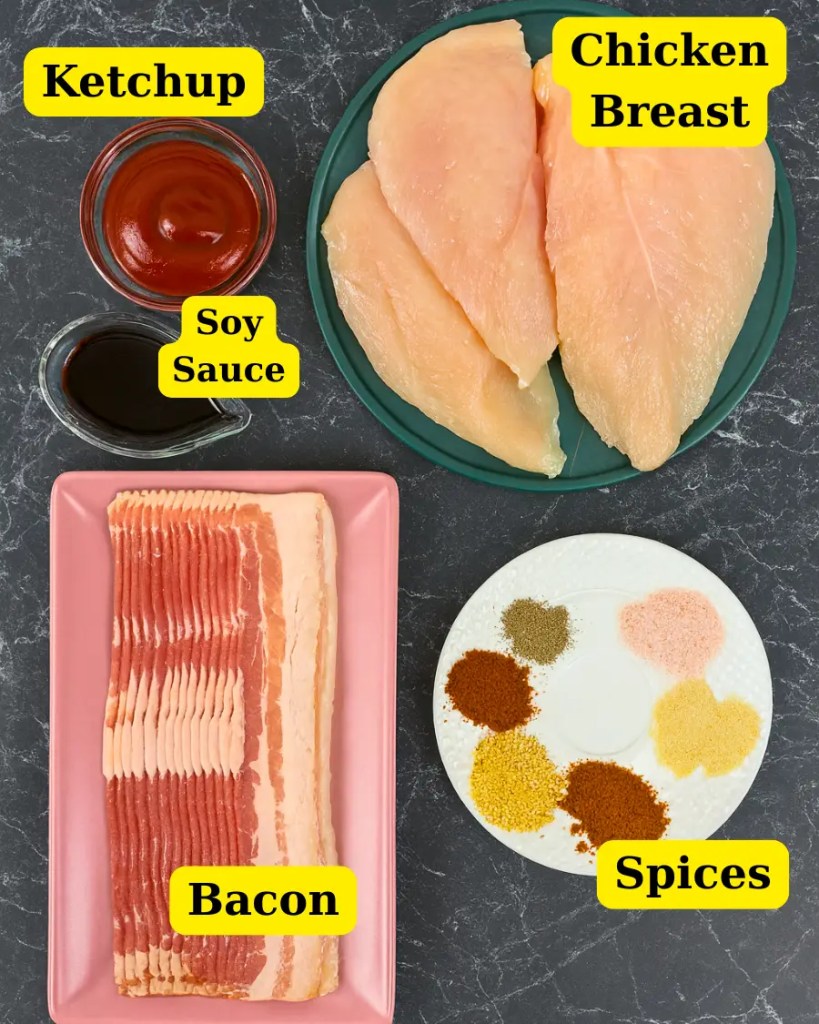 Top view of ingredients for Bacon Wrapped Chicken Skewers, including raw chicken breasts on a green plate, strips of bacon on a pink tray, assorted spices on a white plate, and small bowls of soy sauce and ketchup arranged neatly on a black marble surface.