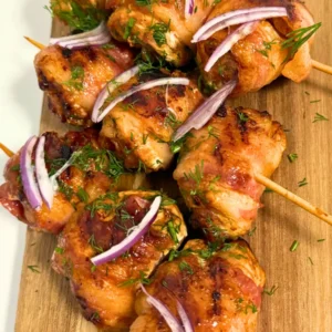 Juicy Bacon Wrapped Chicken Skewers topped with fresh dill and red onion slices, served with tomato dipping sauce.