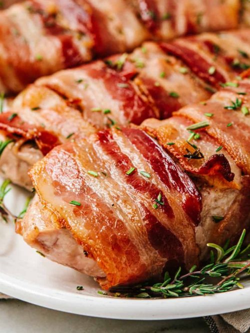 Wrapped in crispy bacon, these juicy, herbaceous Bacon Wrapped Pork Chops are so easy to make in your oven! A couple of simple secrets in this easy recipe guarantee perfect results every time. Perfect date night or dinner party main course.