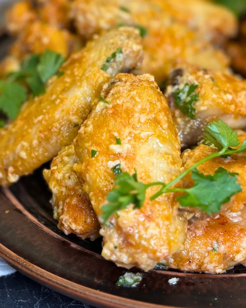 Close-up of juicy crispy chicken wings coated in garlic parmesan butter sauce with parsley garnish