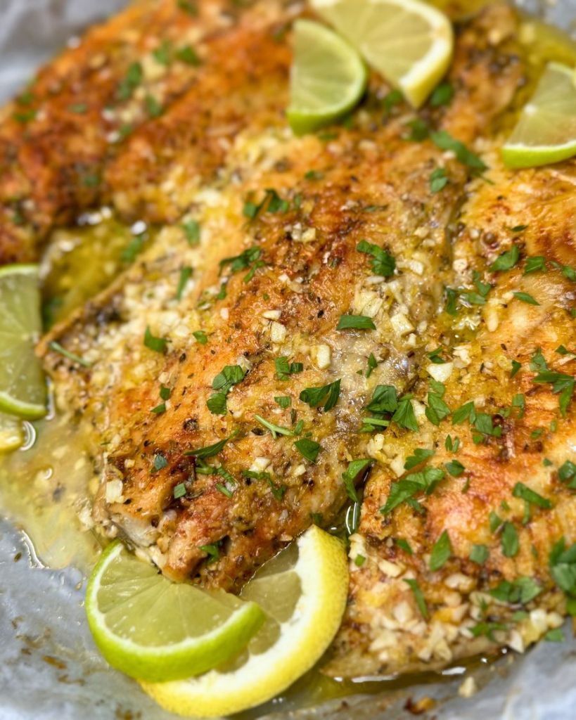 Golden baked cod fillets topped with garlic, parsley, and lemon slices in a buttery sauce.