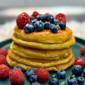 Stack of golden fluffy pancakes topped with raspberries and blueberries, served on a green plate