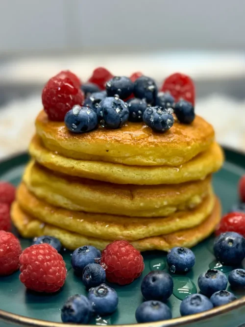 Stack of golden fluffy pancakes topped with raspberries and blueberries, served on a green plate