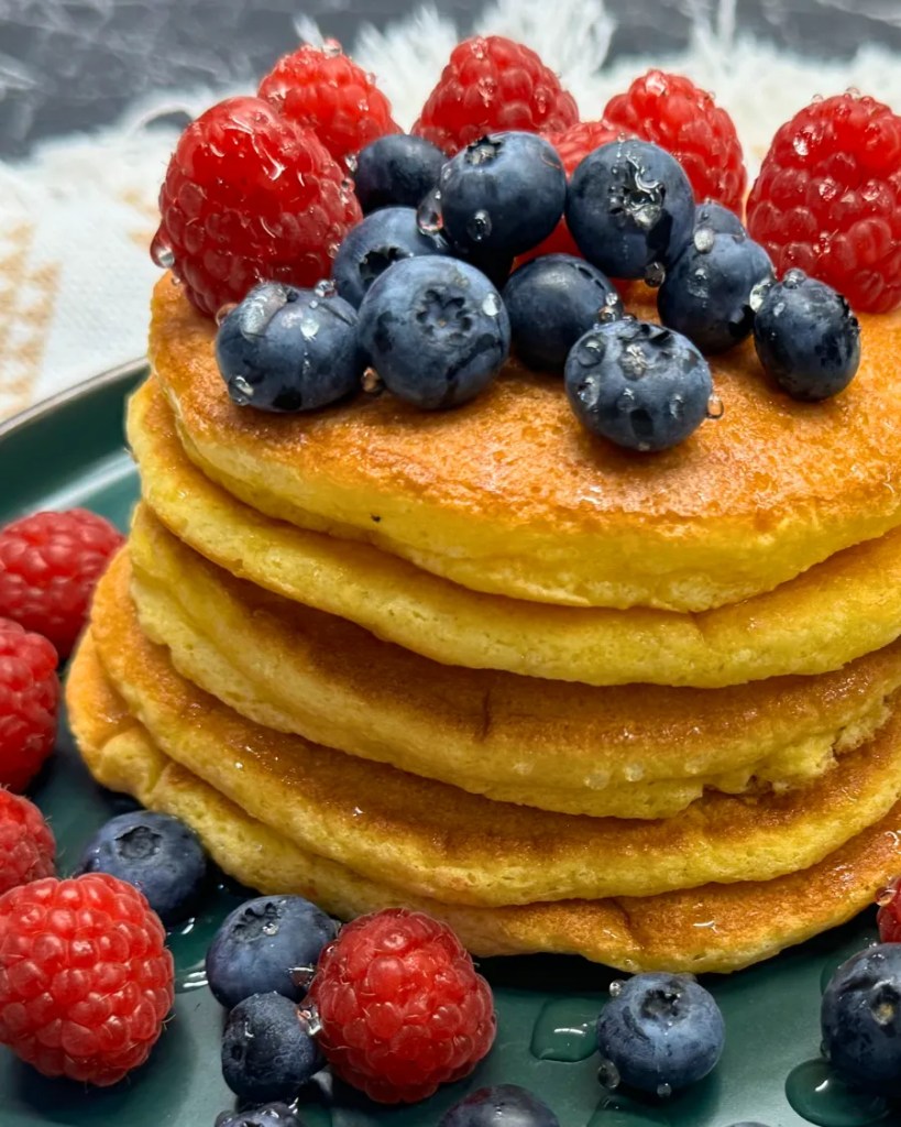 Close-up of fluffy pancakes stacked with fresh blueberries and raspberries on top