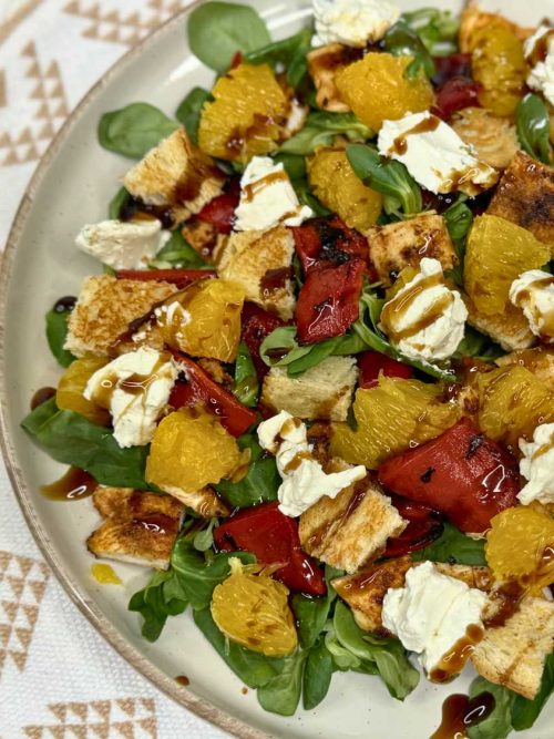 Healthy summer chicken salad with orange, roasted peppers, feta, greens, and balsamic drizzle served on a plate