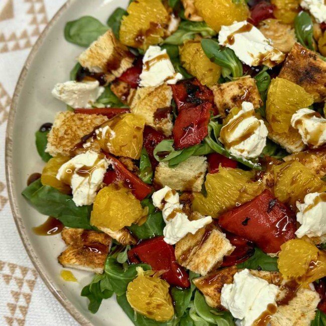 Healthy summer chicken salad with orange, roasted peppers, feta, greens, and balsamic drizzle served on a plate