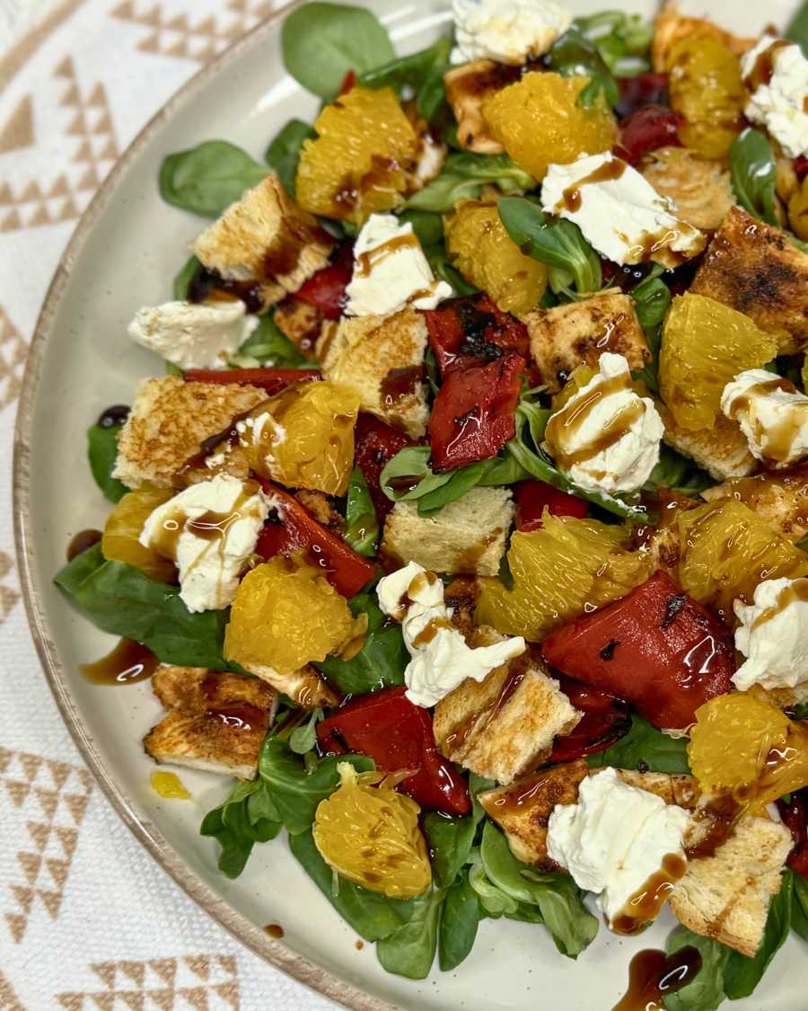 Healthy summer chicken salad with orange, roasted peppers, feta, greens, and balsamic drizzle served on a plate