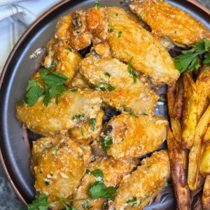 Crispy parmesan garlic butter chicken wings served with fries and fresh orange on a plate
