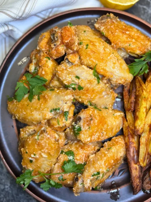 Crispy parmesan garlic butter chicken wings served with fries and fresh orange on a plate