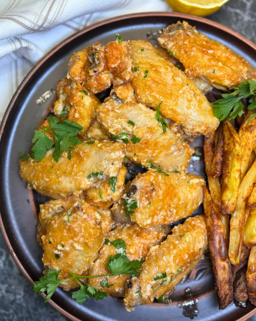 Crispy parmesan garlic butter chicken wings served with fries and fresh orange on a plate