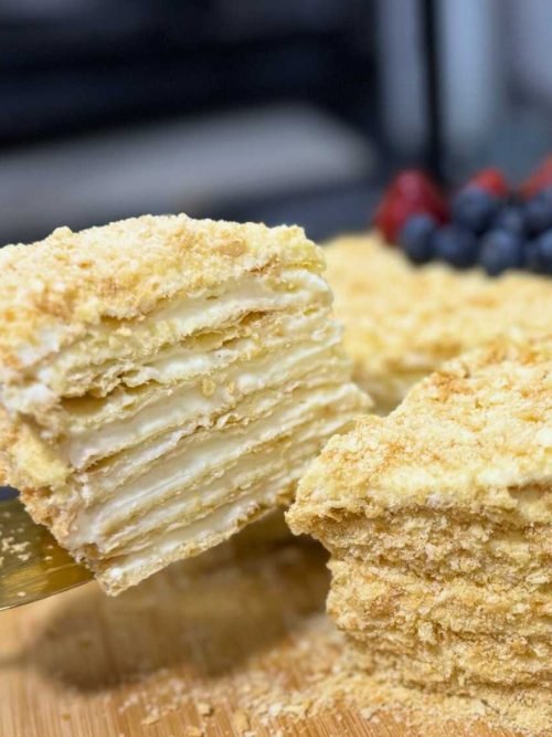 Close-up of a sliced Napoleon Cake with flaky puff pastry layers and creamy custard filling, topped with crushed crumbs.