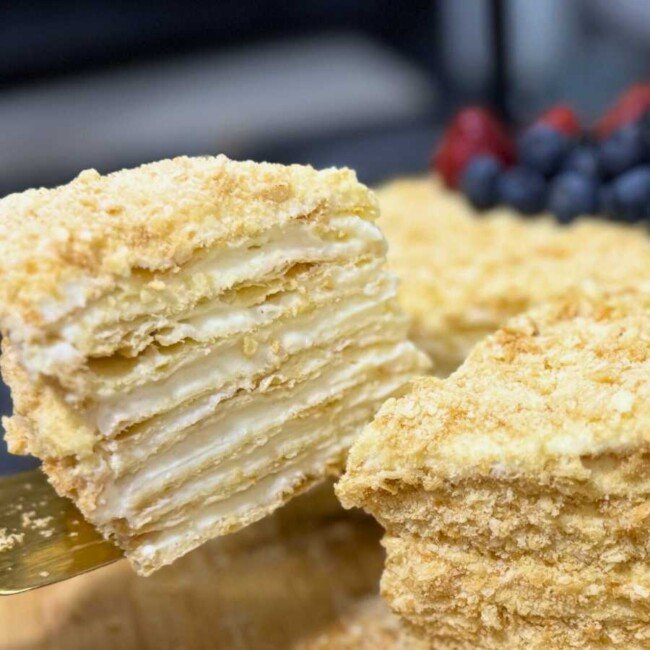 Close-up of a sliced Napoleon Cake with flaky puff pastry layers and creamy custard filling, topped with crushed crumbs.