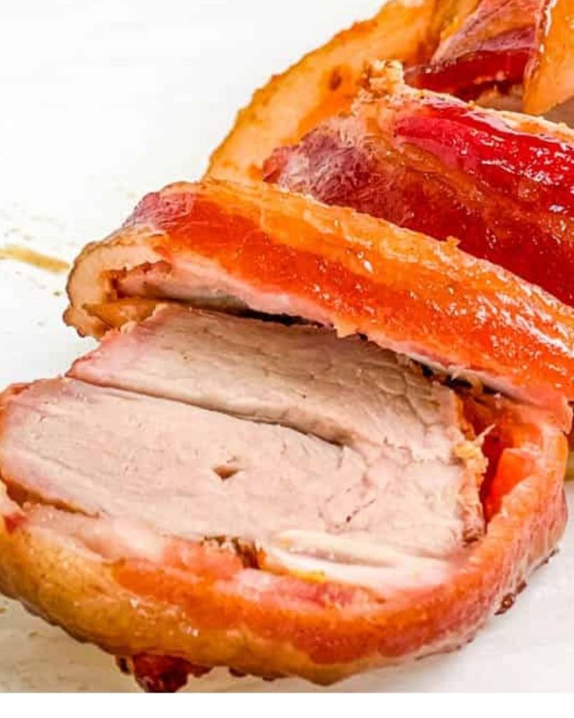Close-up of sliced bacon-wrapped pork tenderloin showing juicy, tender pork and crispy golden bacon.