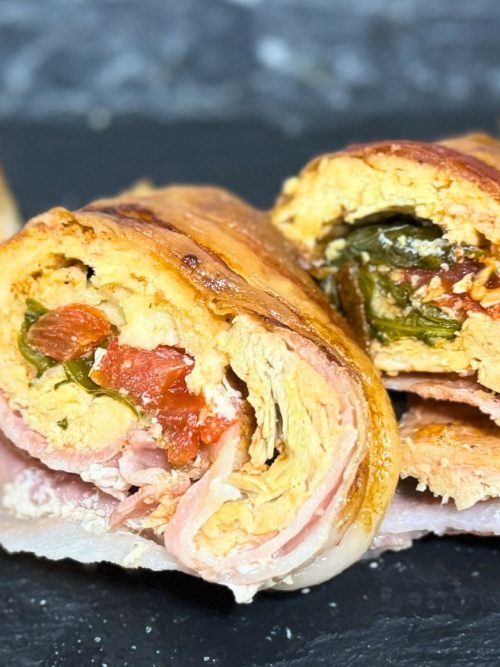 Sliced bacon-wrapped chicken roulade filled with vegetables and herbs, showing the juicy rolled layers and colorful stuffing.