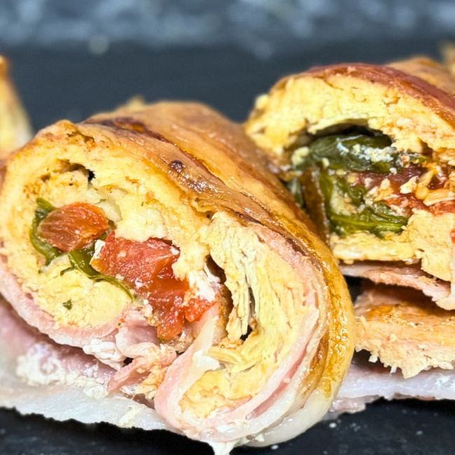 Sliced bacon-wrapped chicken roulade filled with vegetables and herbs, showing the juicy rolled layers and colorful stuffing.