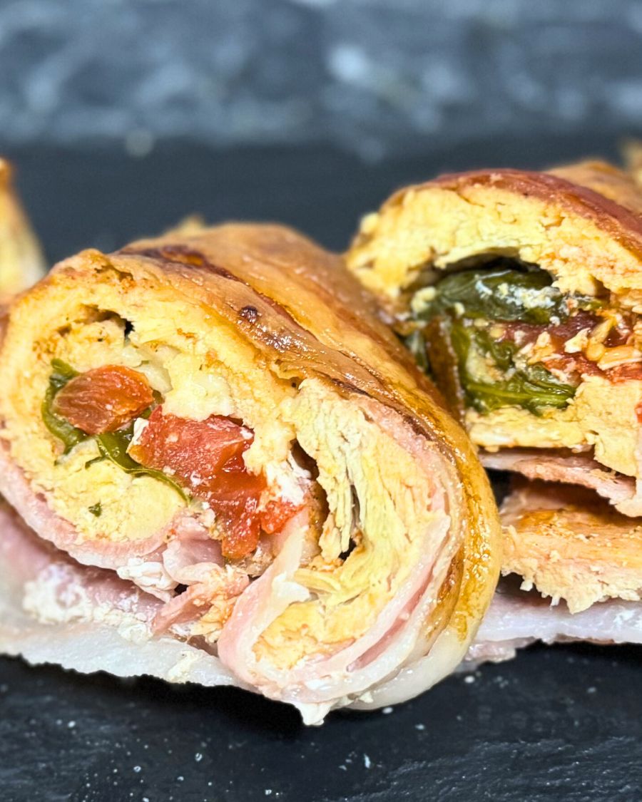 Sliced bacon-wrapped chicken roulade filled with vegetables and herbs, showing the juicy rolled layers and colorful stuffing.