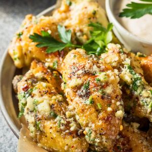 Close-up of crispy Parmesan garlic wings coated in citrus butter glaze, topped with parsley and served with dipping sauce.