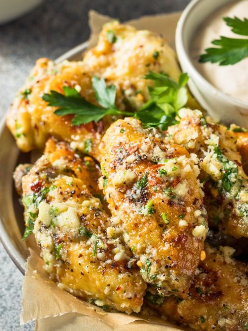 Close-up of crispy Parmesan garlic wings coated in citrus butter glaze, topped with parsley and served with dipping sauce.