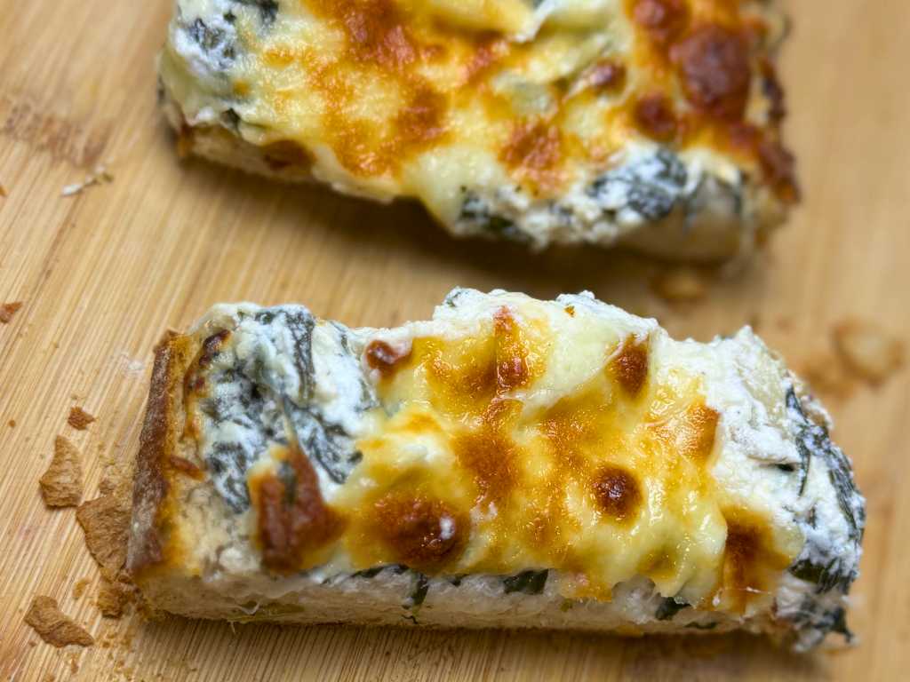 Two slices of spinach artichoke pull-apart bread with creamy filling and golden melted cheese on a wooden board.