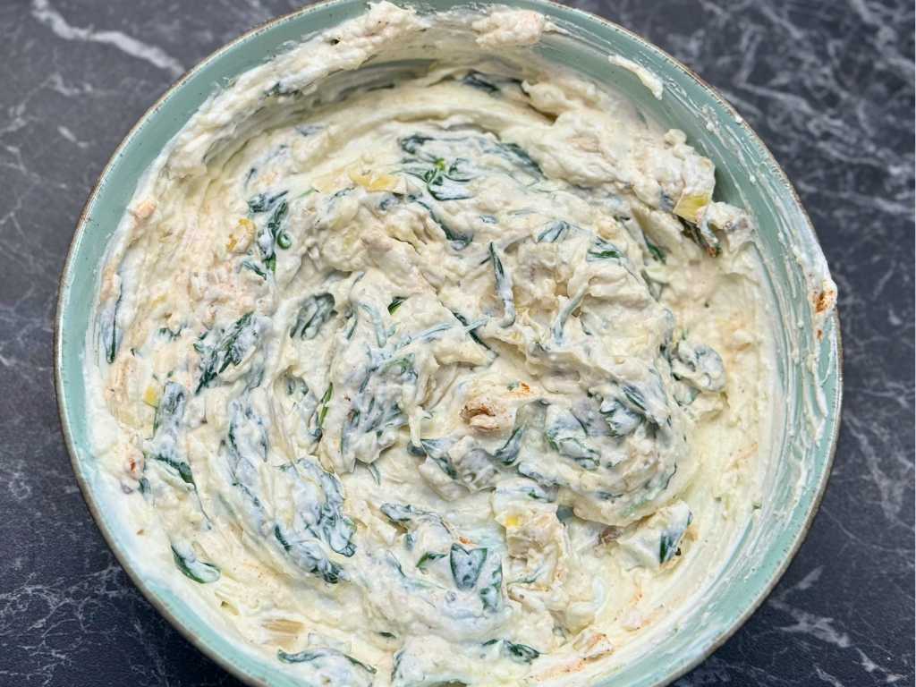 Bowl of creamy spinach and artichoke cheese mixture, ready to be stuffed into sourdough bread for baking.