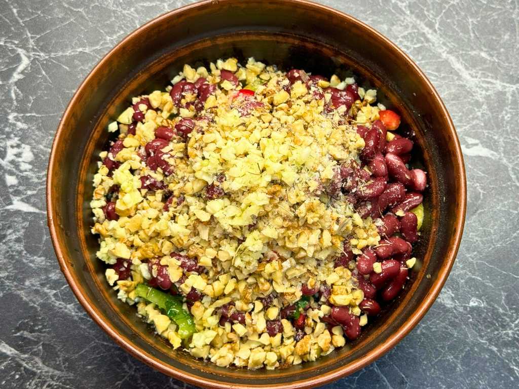 Chopped walnuts added to a bowl of beans, peppers, and herbs for Tbilisi Salad.