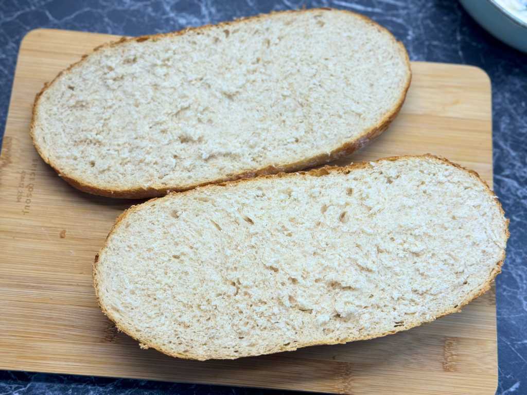 Two sourdough bread halves placed on a wooden cutting board, ready to be filled with spinach artichoke cheese mixture.
