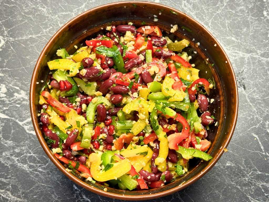 Mixed Tbilisi Salad with beans, pomegranate, walnuts, bell peppers, and fresh herbs in a brown bowl.