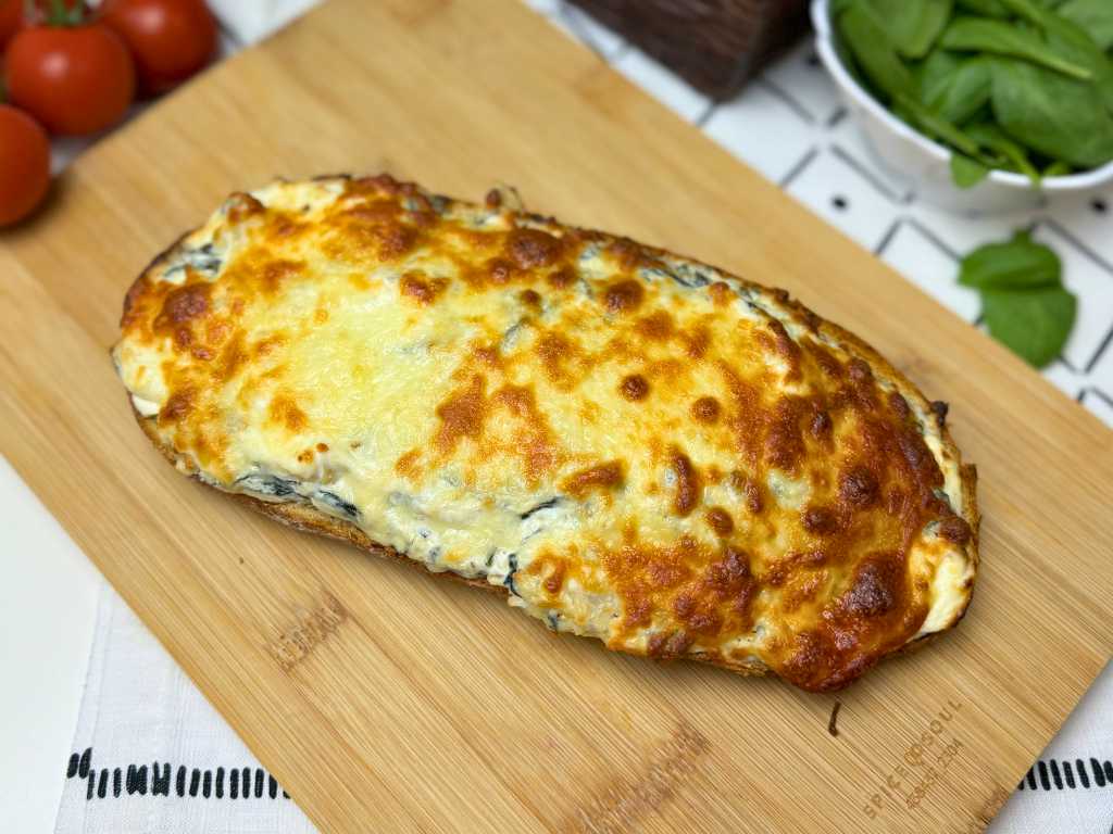Freshly baked spinach artichoke pull-apart bread with golden, bubbly cheese on top, resting on a wooden cutting board.