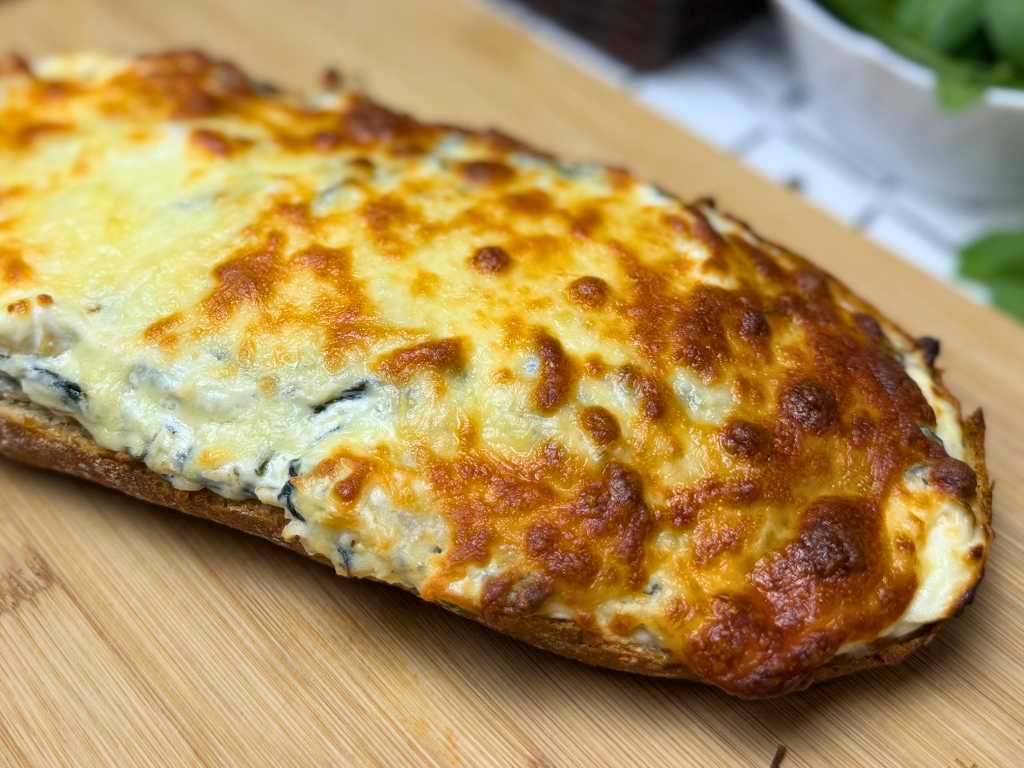 Close-up view of spinach artichoke pull-apart bread with a golden, bubbly cheese topping, resting on a wooden cutting board.