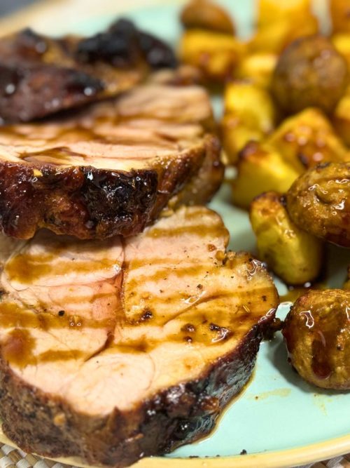 Close-up of juicy pork tenderloin slices with honey soy glaze, served alongside golden roasted potatoes and mushrooms on a plate