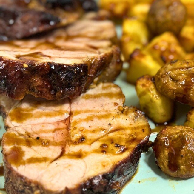Close-up of juicy pork tenderloin slices with honey soy glaze, served alongside golden roasted potatoes and mushrooms on a plate