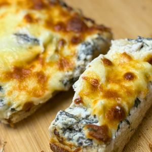 Close-up of golden baked spinach artichoke pull-apart bread with melted mozzarella and creamy filling on a wooden board.