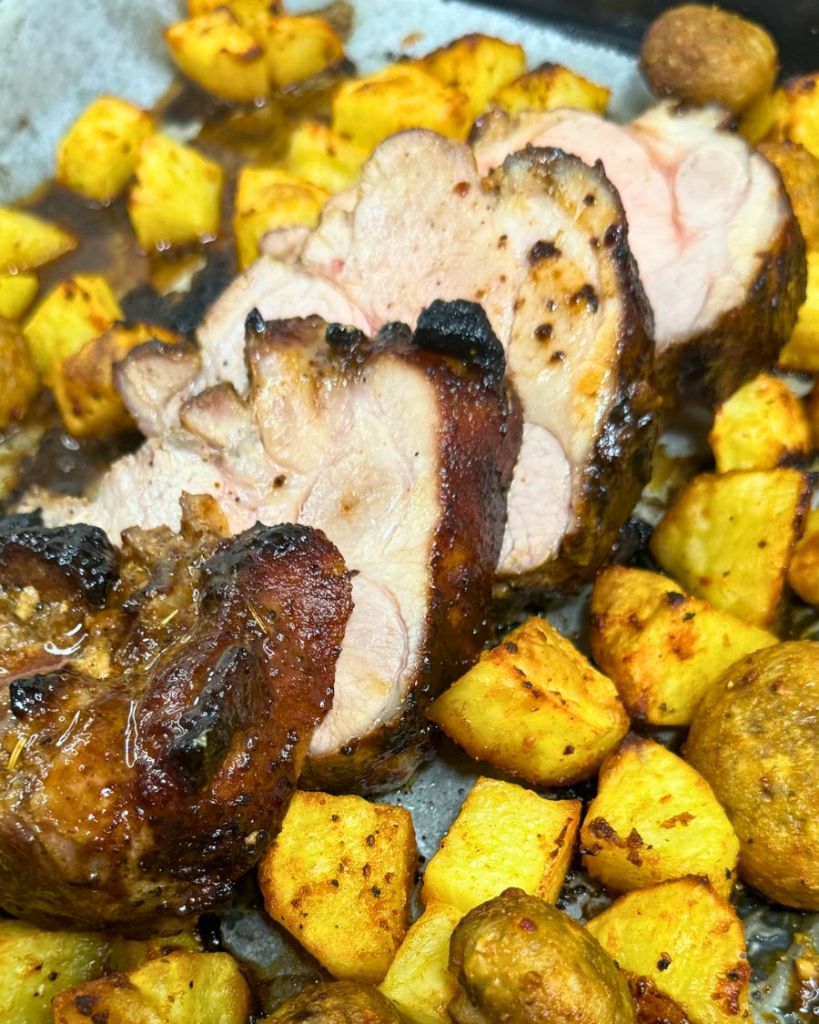 Juicy sliced pork tenderloin with golden roasted potatoes and mushrooms on a baking tray.