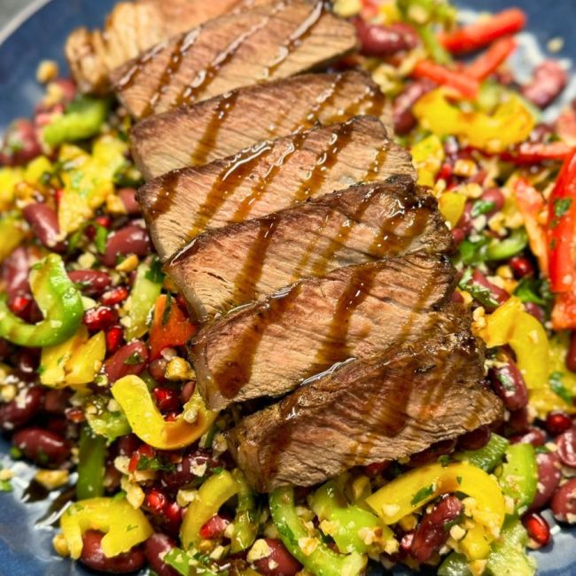 Sliced beef served over colorful Tbilisi Salad with pomegranate, walnuts, beans, and fresh herbs, drizzled with dressing.