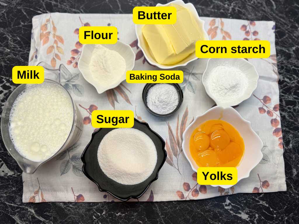 Spartak Cake cream ingredients labeled: milk, sugar, butter, flour, cornstarch, baking soda, and egg yolks arranged on a floral cloth.