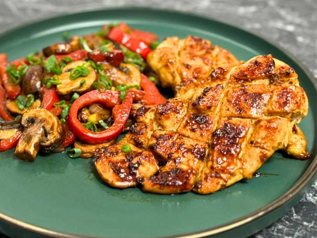 Golden, caramelized Asian-style chicken breasts served with sautéed bell peppers, mushrooms, onions, and fresh green onions on a green plate.
