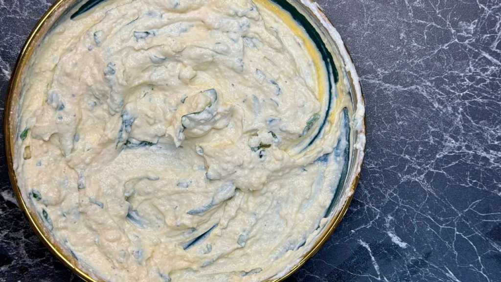 Bowl of creamy ricotta cheese mixture with herbs, ready to be used as filling for zucchini lasagna.