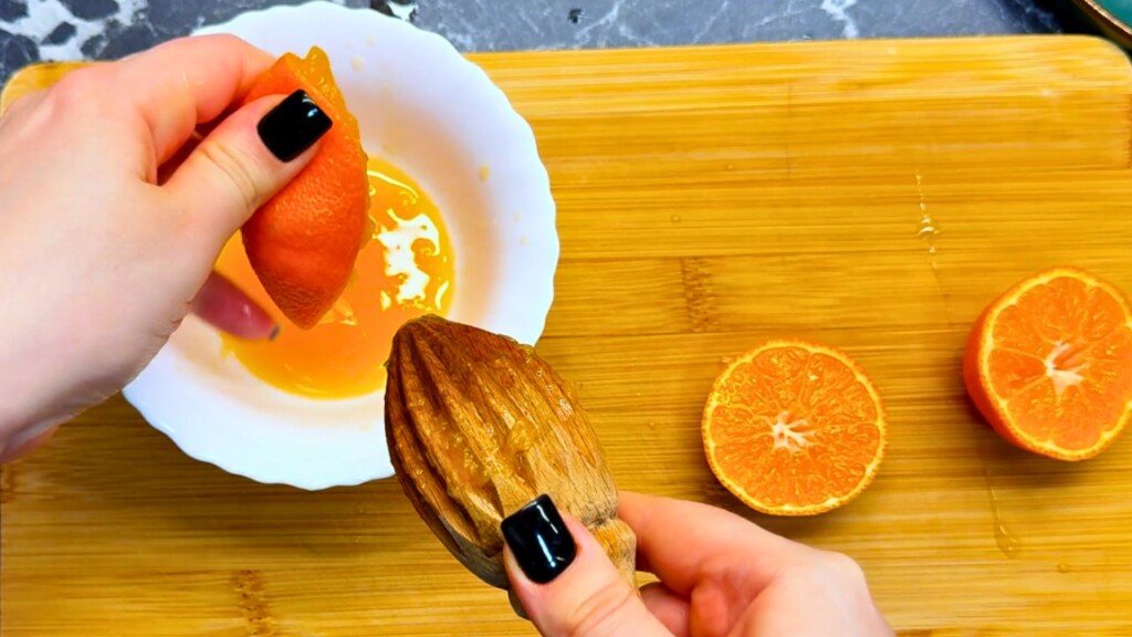 Hand squeezing fresh clementine juice with a wooden reamer into a white bowl on a wooden cutting board—perfect for citrus glaze in a honey orange duck breast recipe.