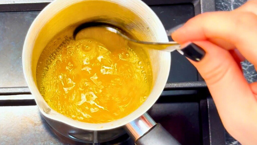 Close-up of a hand stirring golden honey-orange glaze in a saucepan on the stove, showing the bubbling citrus mixture used for duck breast recipes.